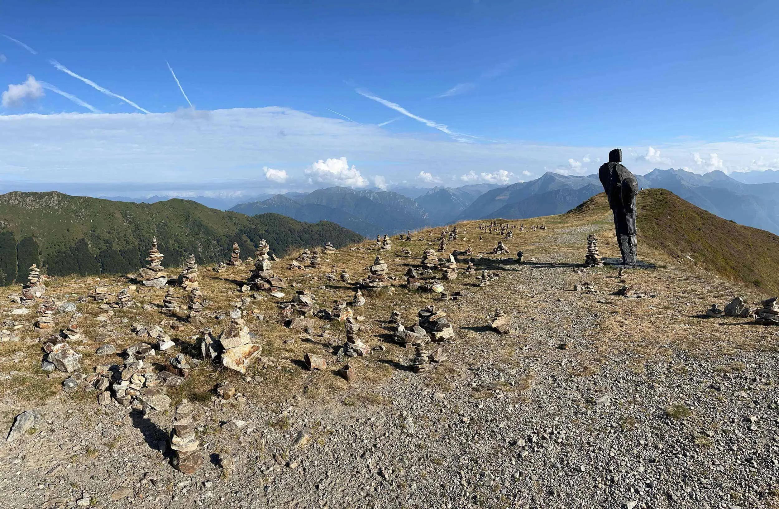 Berglandschaft mit zahlreichen kleinen Steintürmen, einem großen Holztotem und weitem Himmel mit Wolken.