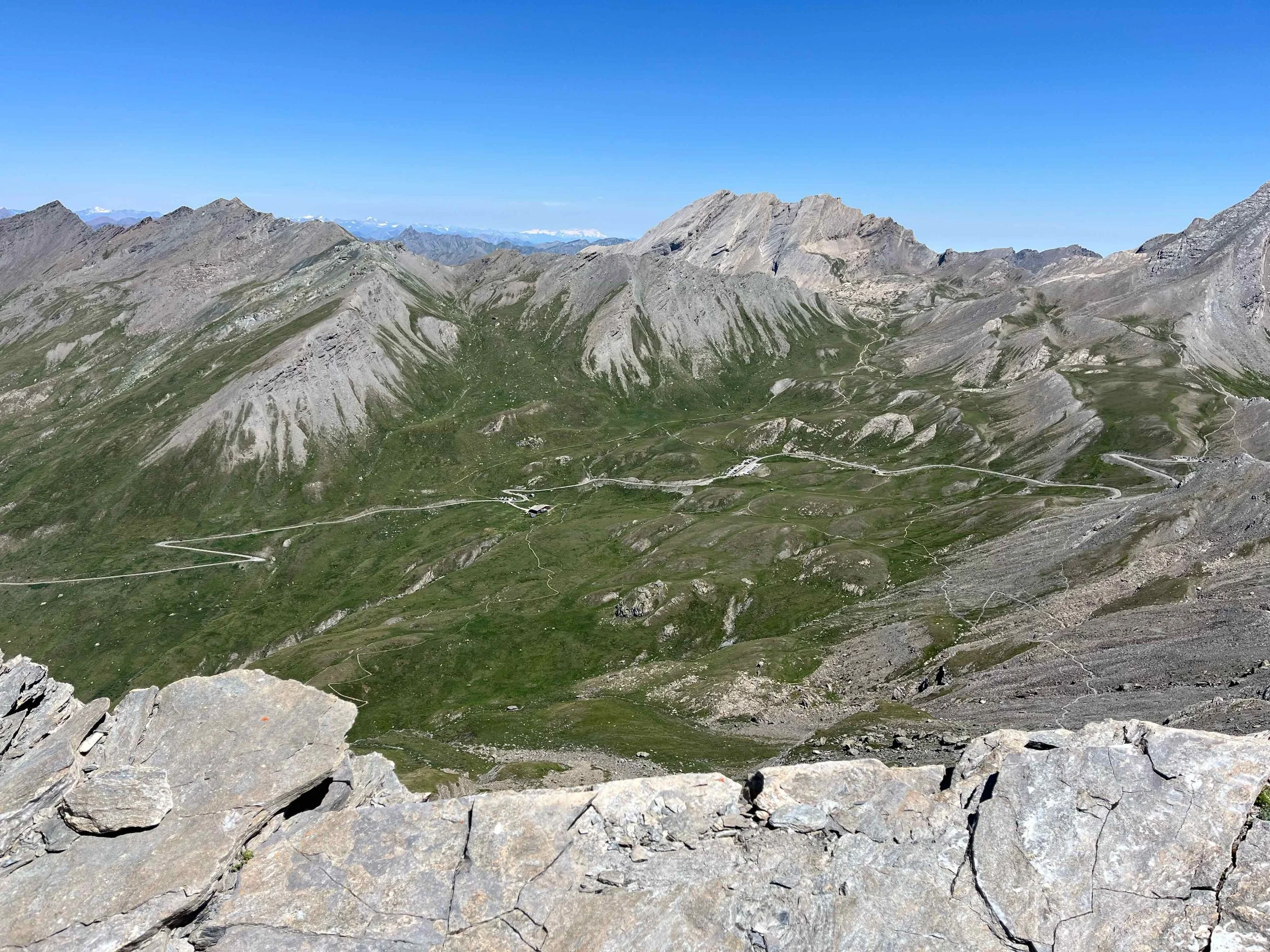 Berglandschaft mit grünem Tal, steilen Felsen und schmalen Wegen, unter klarem blauen Himmel.