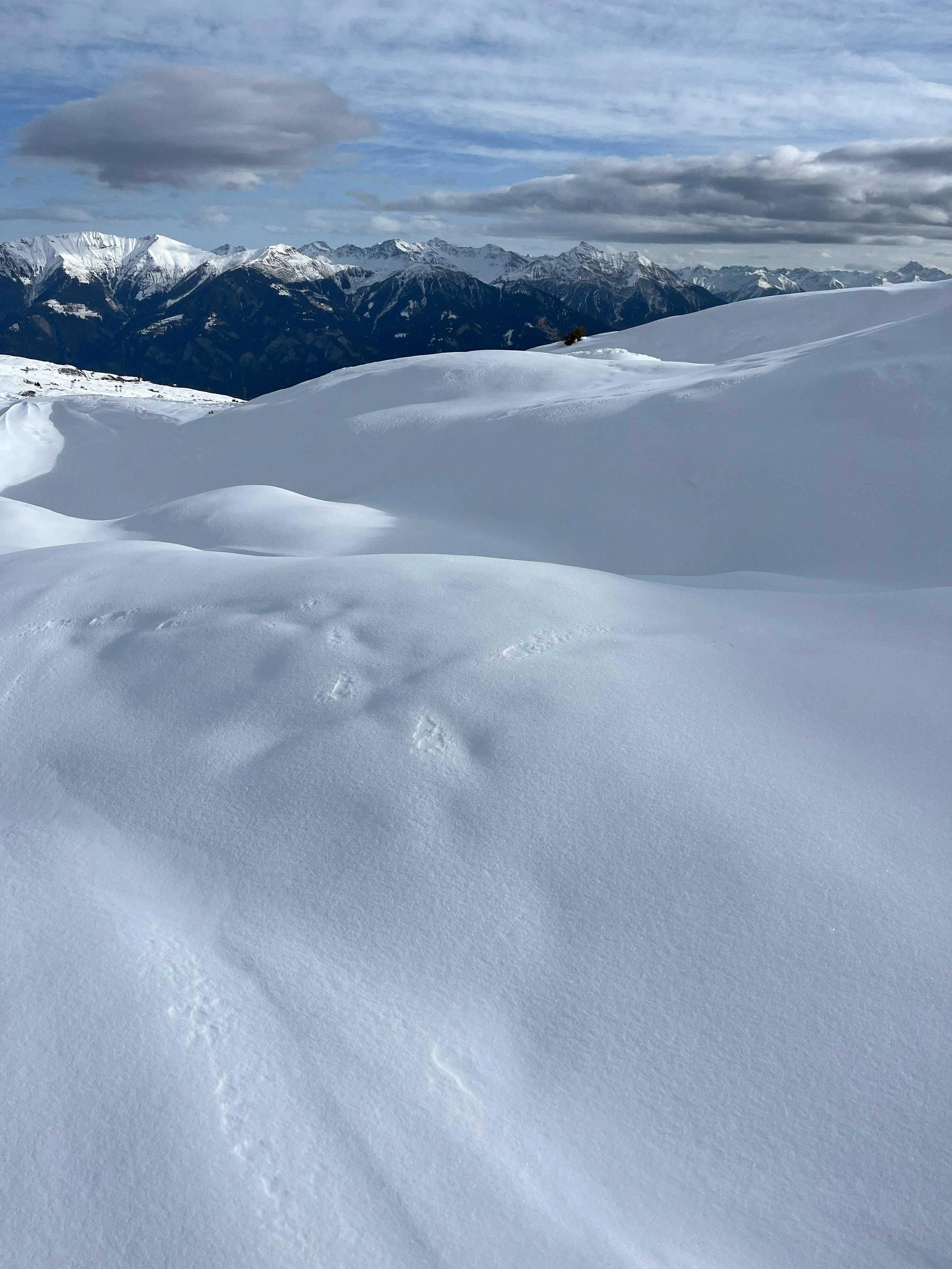 Schnee bedeckter Berglandschaft mit Wolken am Himmel.