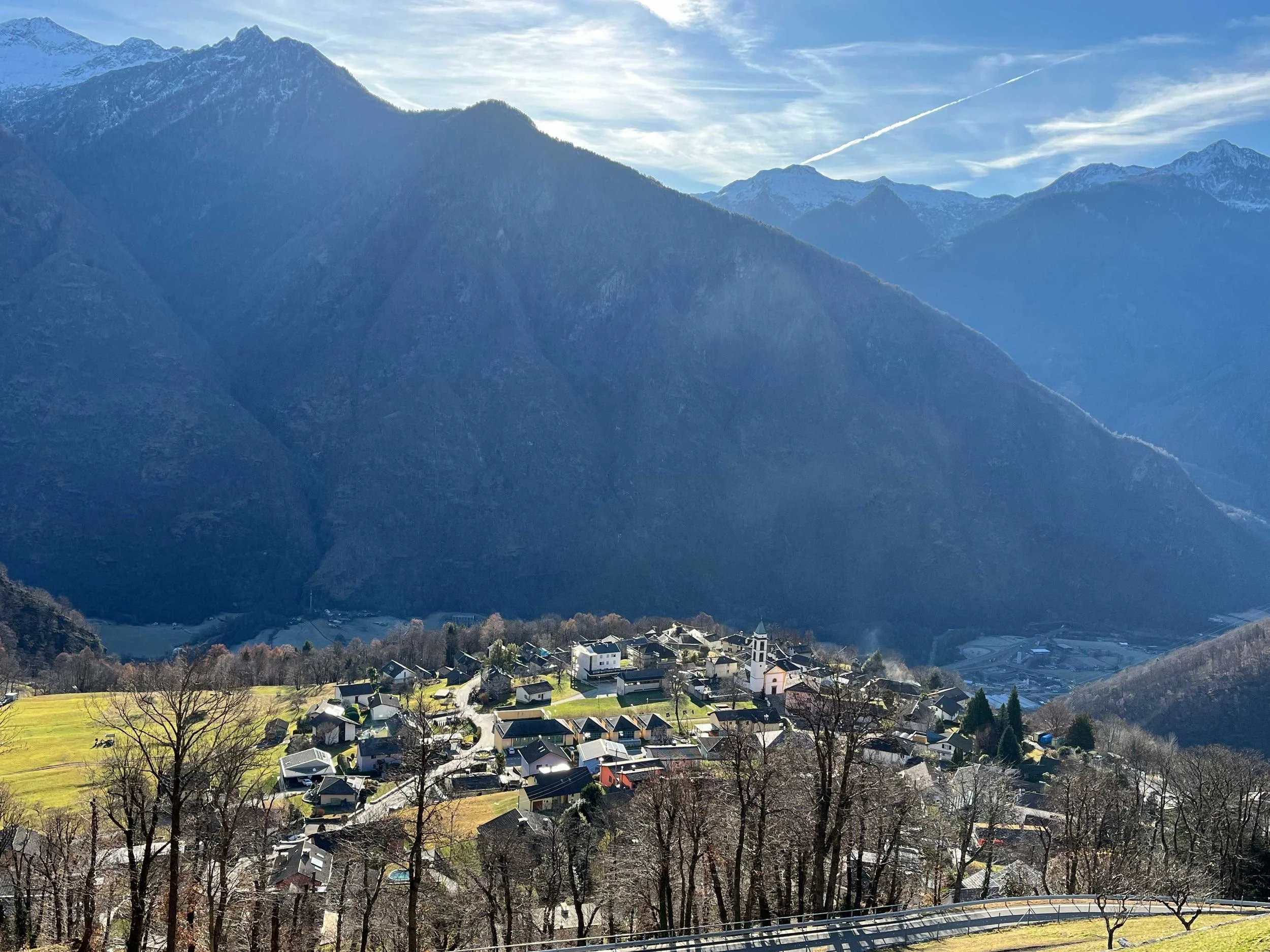 Ein malerisches Dorf im Tal, umgeben von hohen, schneebedeckten Bergen, bei strahlendem Sonnenschein.
