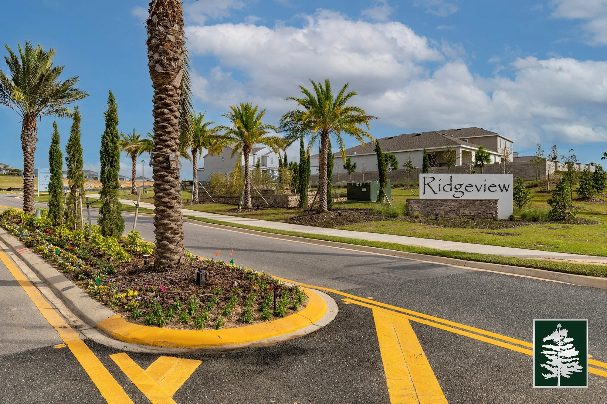 Entrance to Ridgeview residential community with palm trees, landscaped greenery, and a sign that reads 'Ridgeview' against a partly cloudy sky.