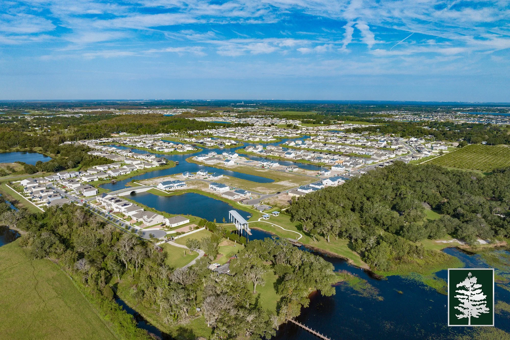 Aerial view of a residential neighborhood with multiple lakes and waterways, surrounded by greenery and trees under a blue sky.