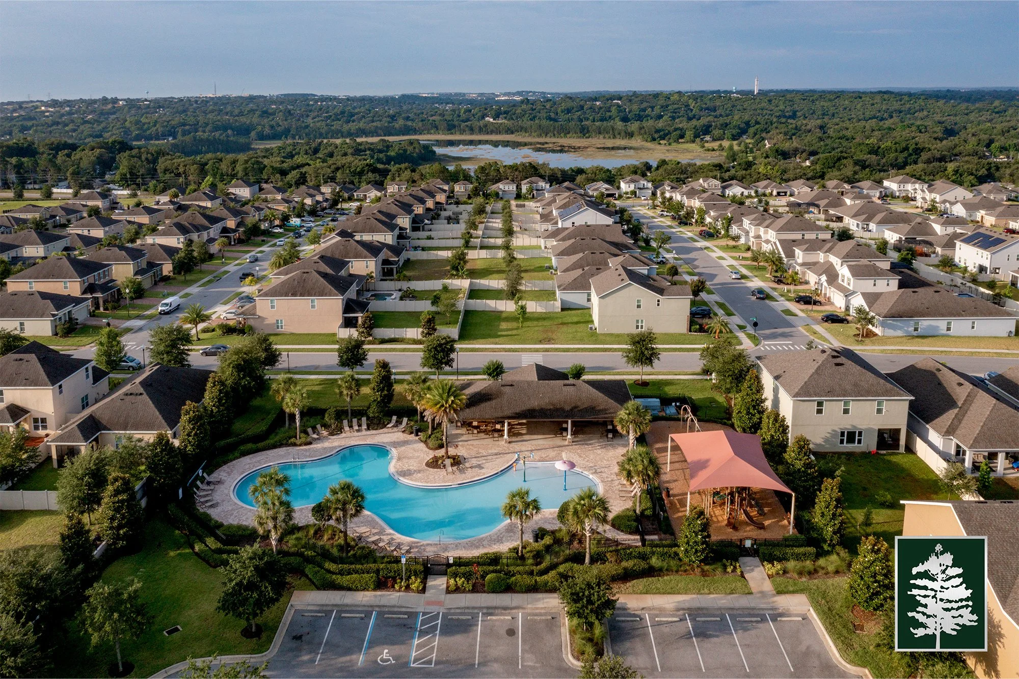 Aerial view of a residential neighborhood with a community swimming pool, clubhouse, and surrounding houses with well-maintained yards and trees.