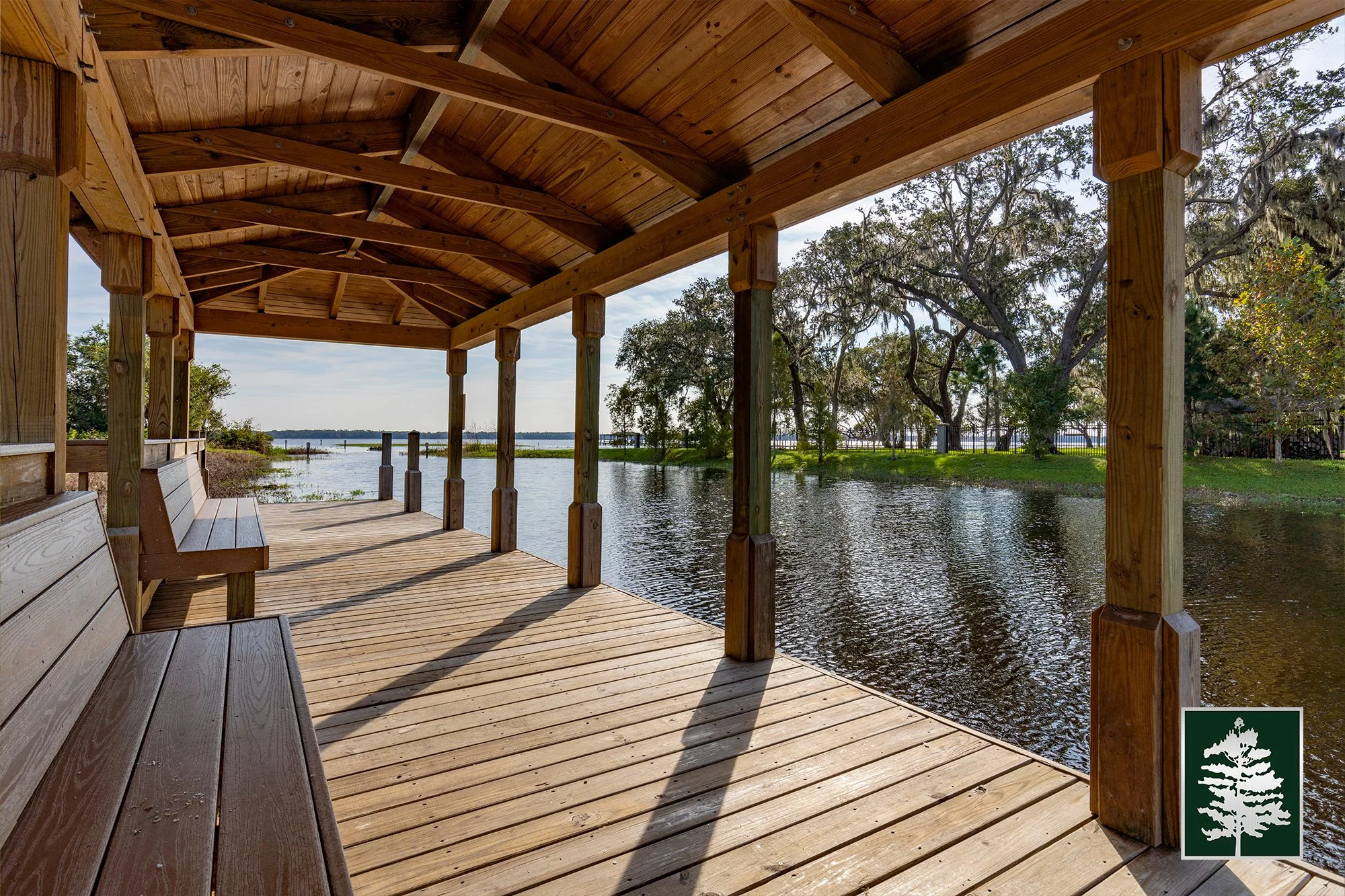 Wooden gazebo with benches overlooking a river and trees on a sunny day.