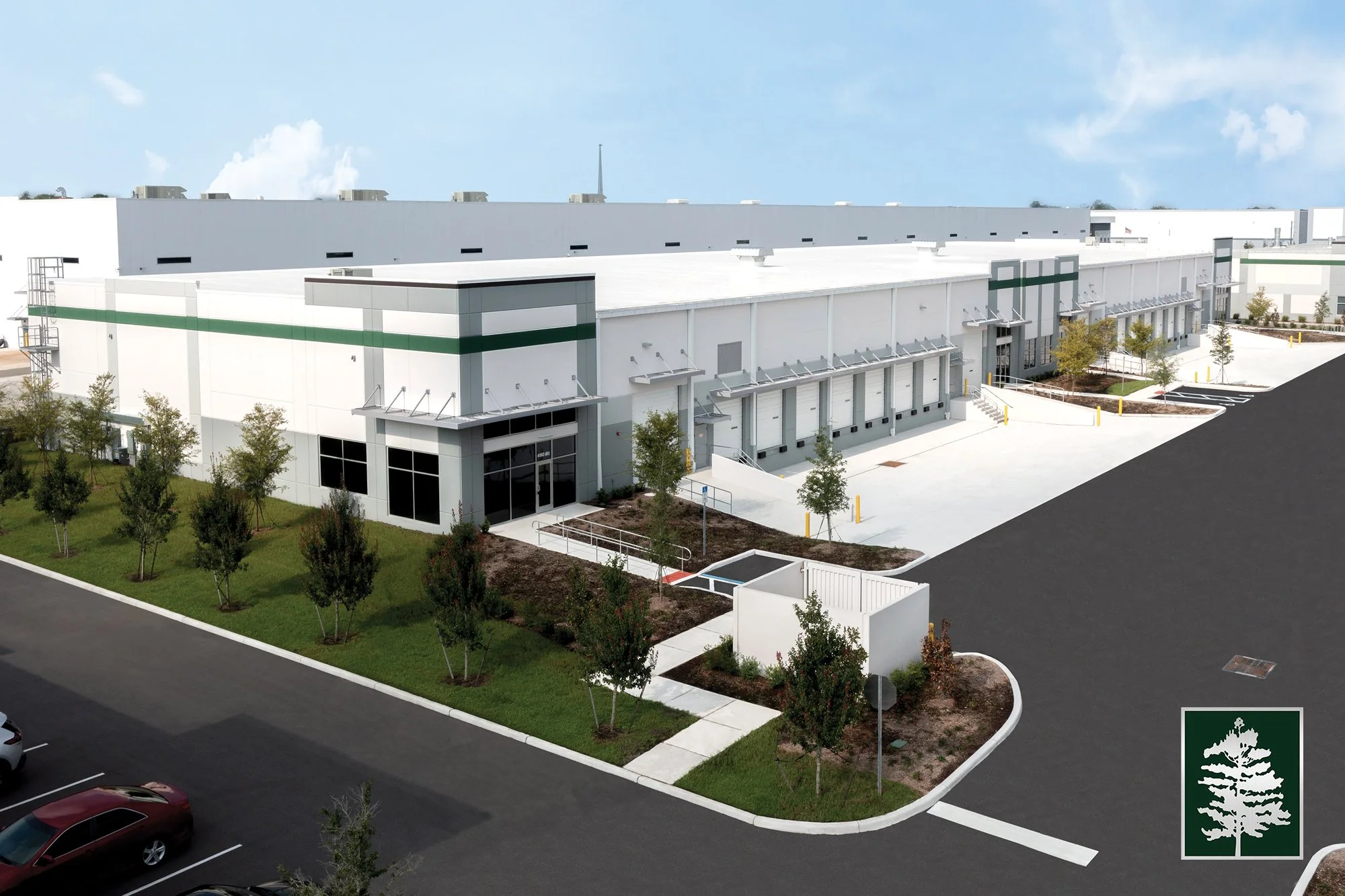 A large modern warehouse with loading docks and parking lot, landscaped with small trees and grass areas.