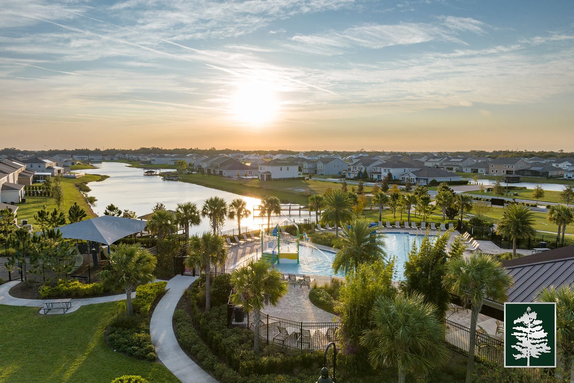 Sunset over a residential community with a swimming pool, palm trees, walking paths, and a waterway with houses in the background.