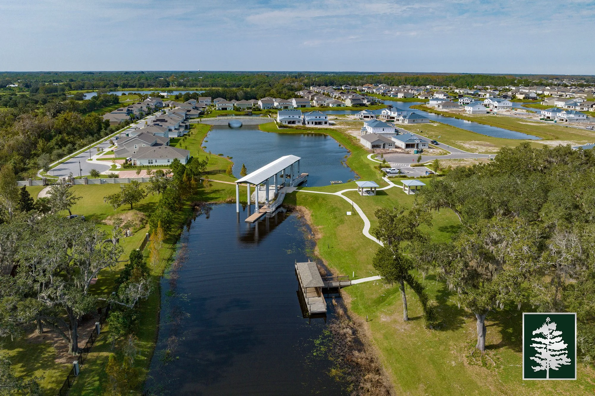 Aerial view of a residential community with houses, green lawns, ponds, and walking paths, including a pier and boat dock.