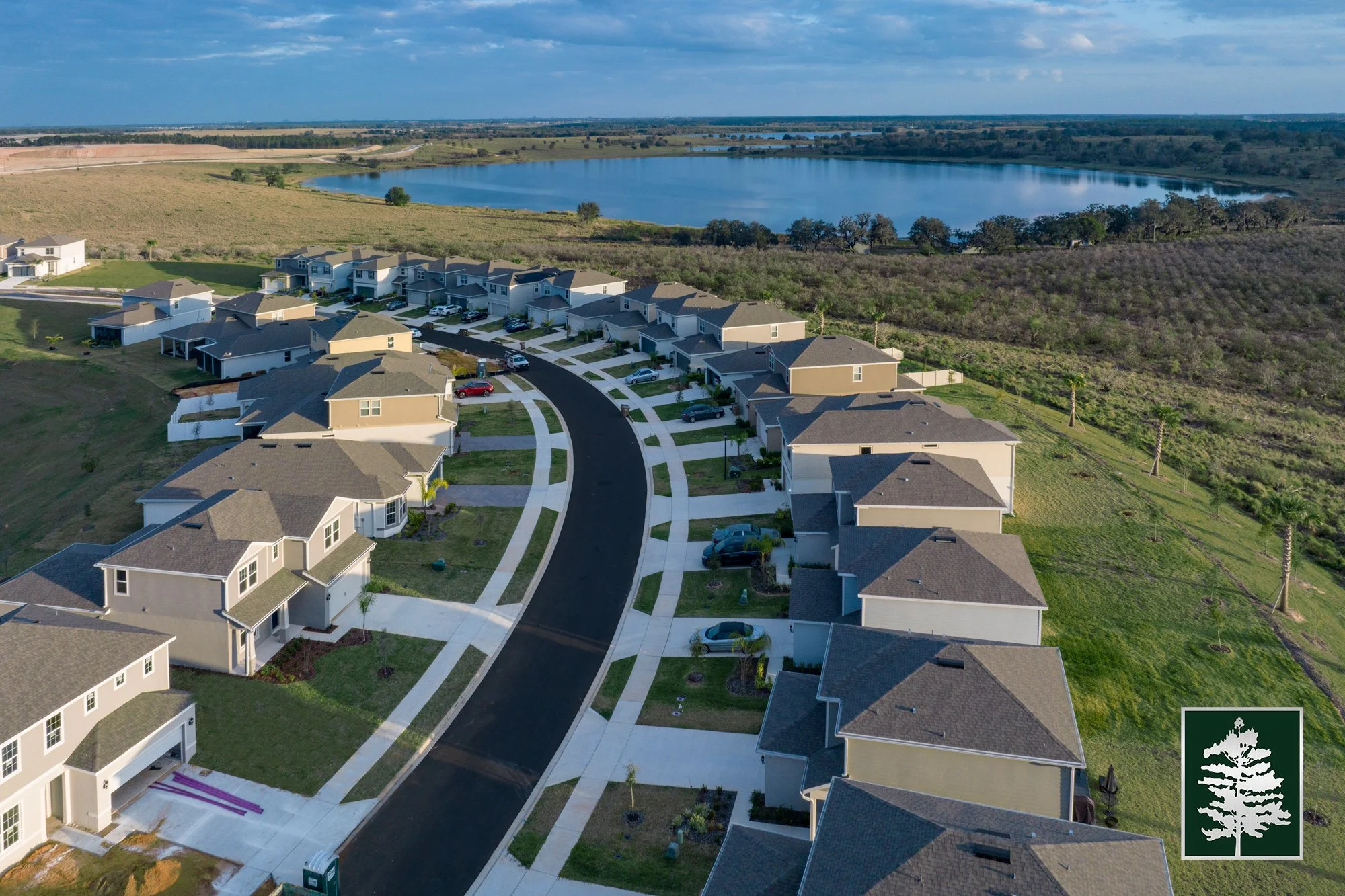 Aerial view of a suburban neighborhood with new houses, a curved street, and a nearby lake in the background.