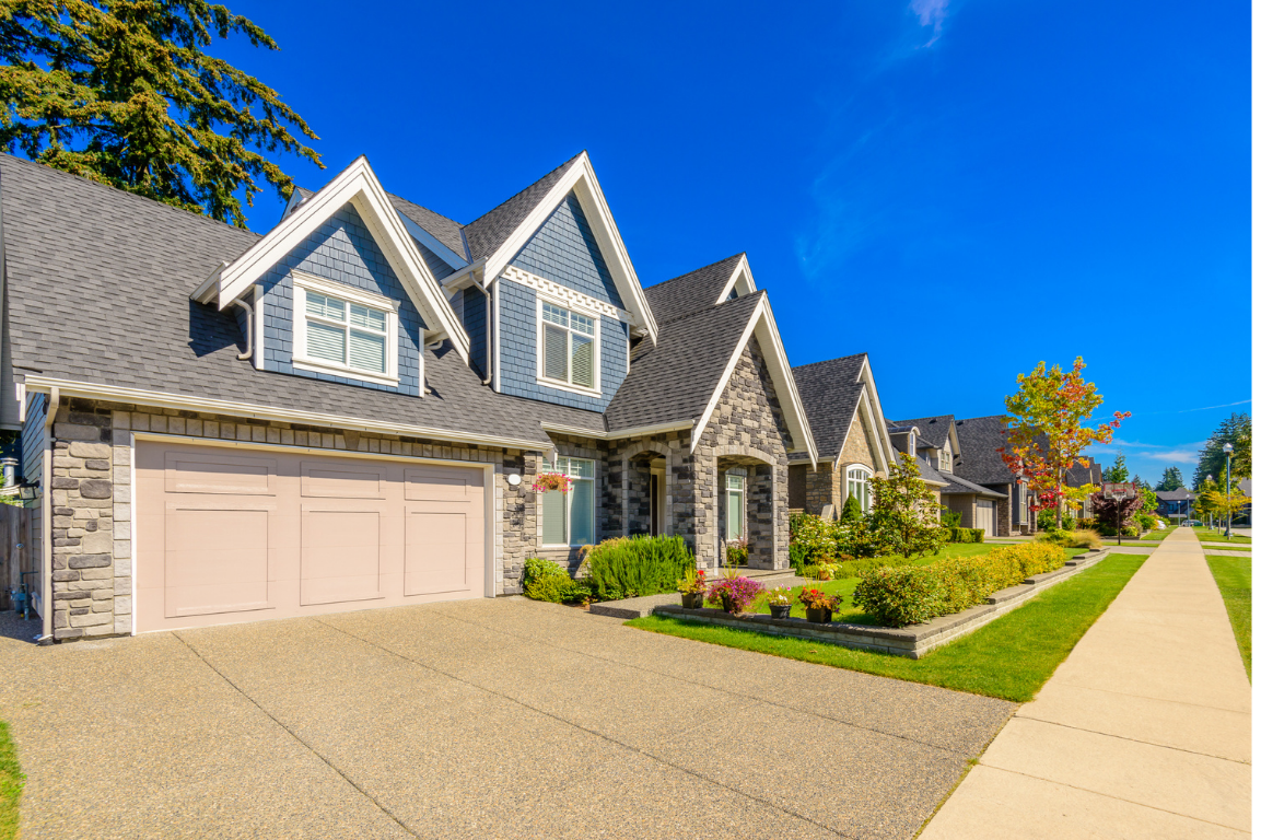 Suburban neighborhood with a row of modern houses, well-maintained front yards, and a sidewalk under a clear blue sky.