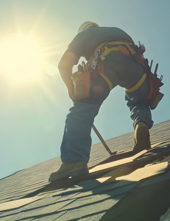 A construction worker on a roof, wearing a safety harness and helmet, working under the bright sun.