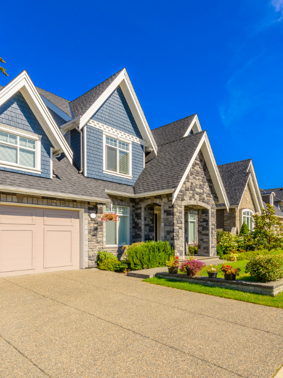 A modern suburban house with blue and gray siding, a pink garage door, and a well-maintained front yard with flowers and shrubs under a clear blue sky.
