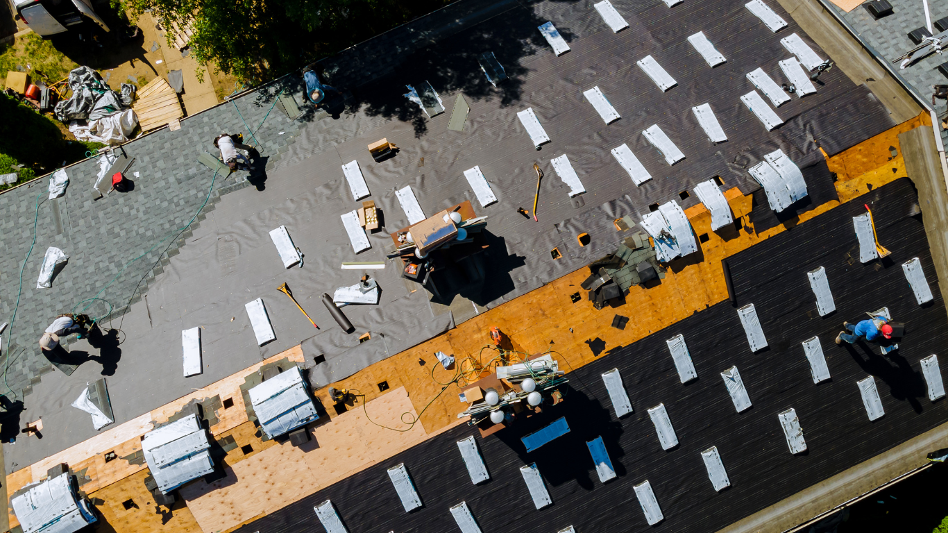 Aerial view of a roofing crew working on installing solar panels on a flat roof with multiple rows of solar panels partially installed and workers in safety gear.