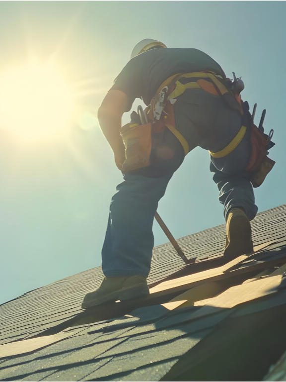 A construction worker wearing a safety helmet and harness is working on a roof under the sunlight.