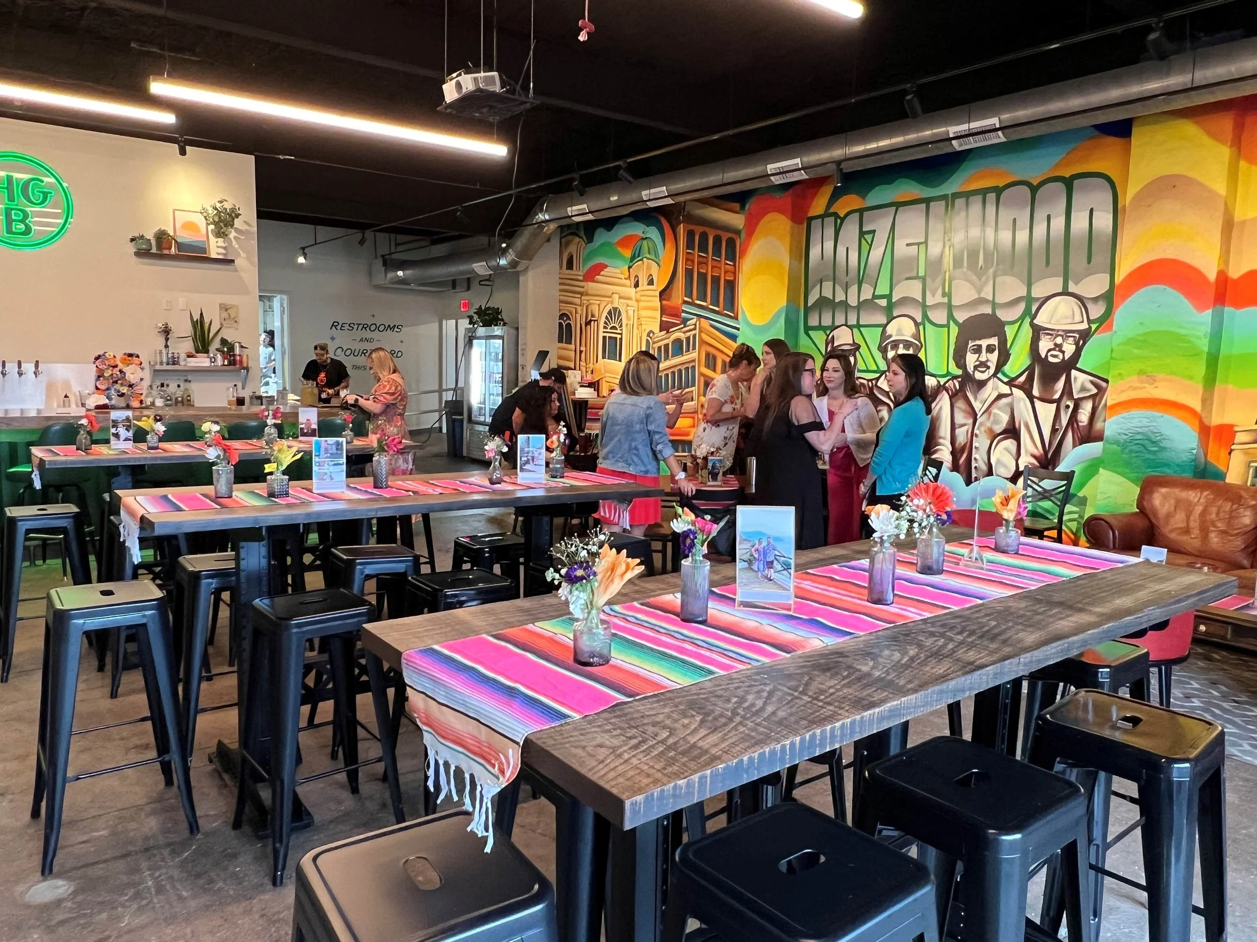 Hazel Grove Brewing's colorful taproom with mural art decorated for a private event with a group of people standing and chatting near the mural.