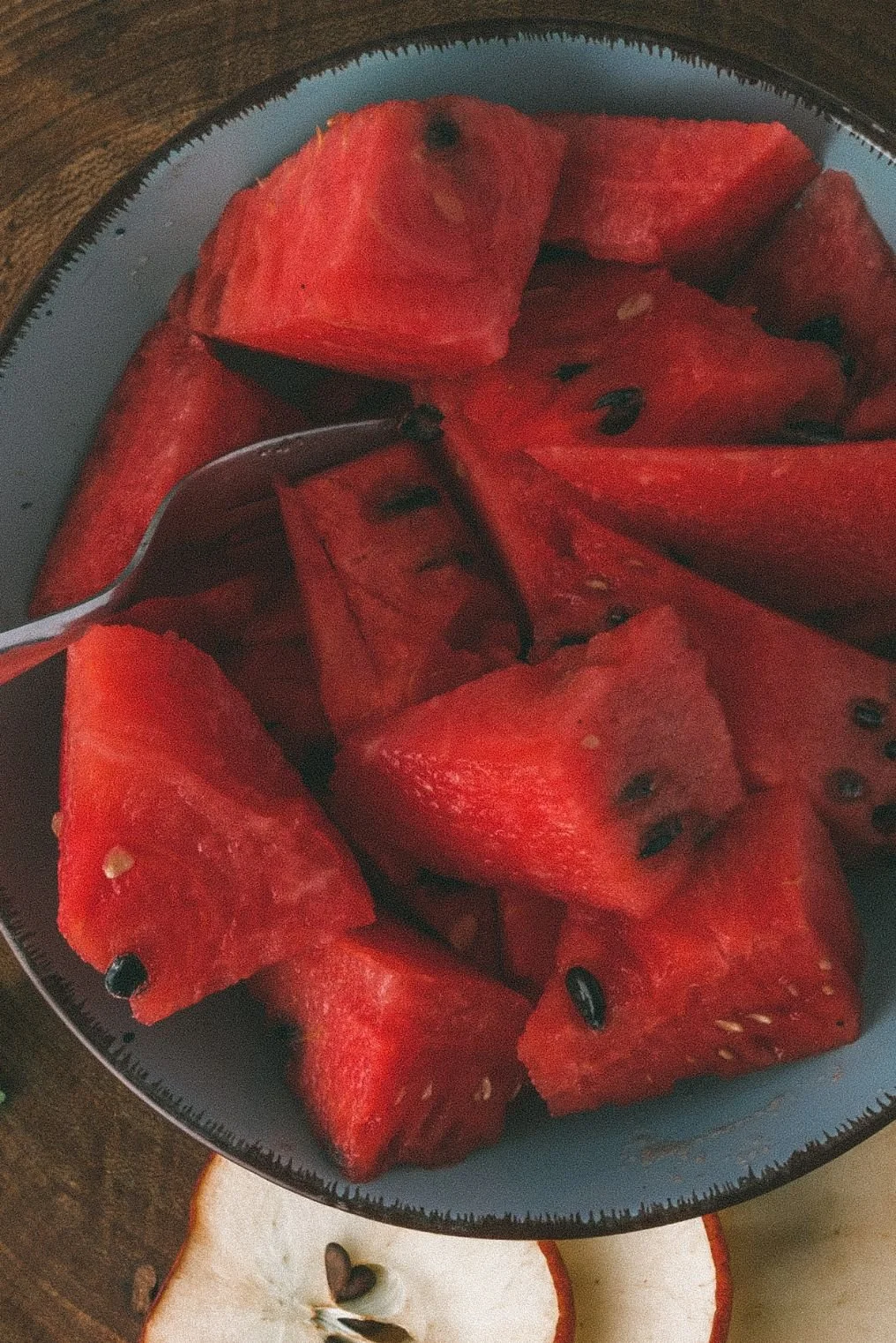 A bowl filled with cut pieces of bright red watermelon with black seeds, with a fork partially inserted into the fruit.