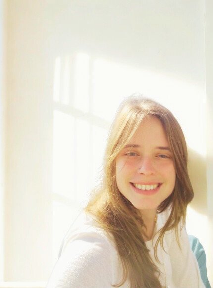 Young woman smiling with sunlight streaming through a window in the background.