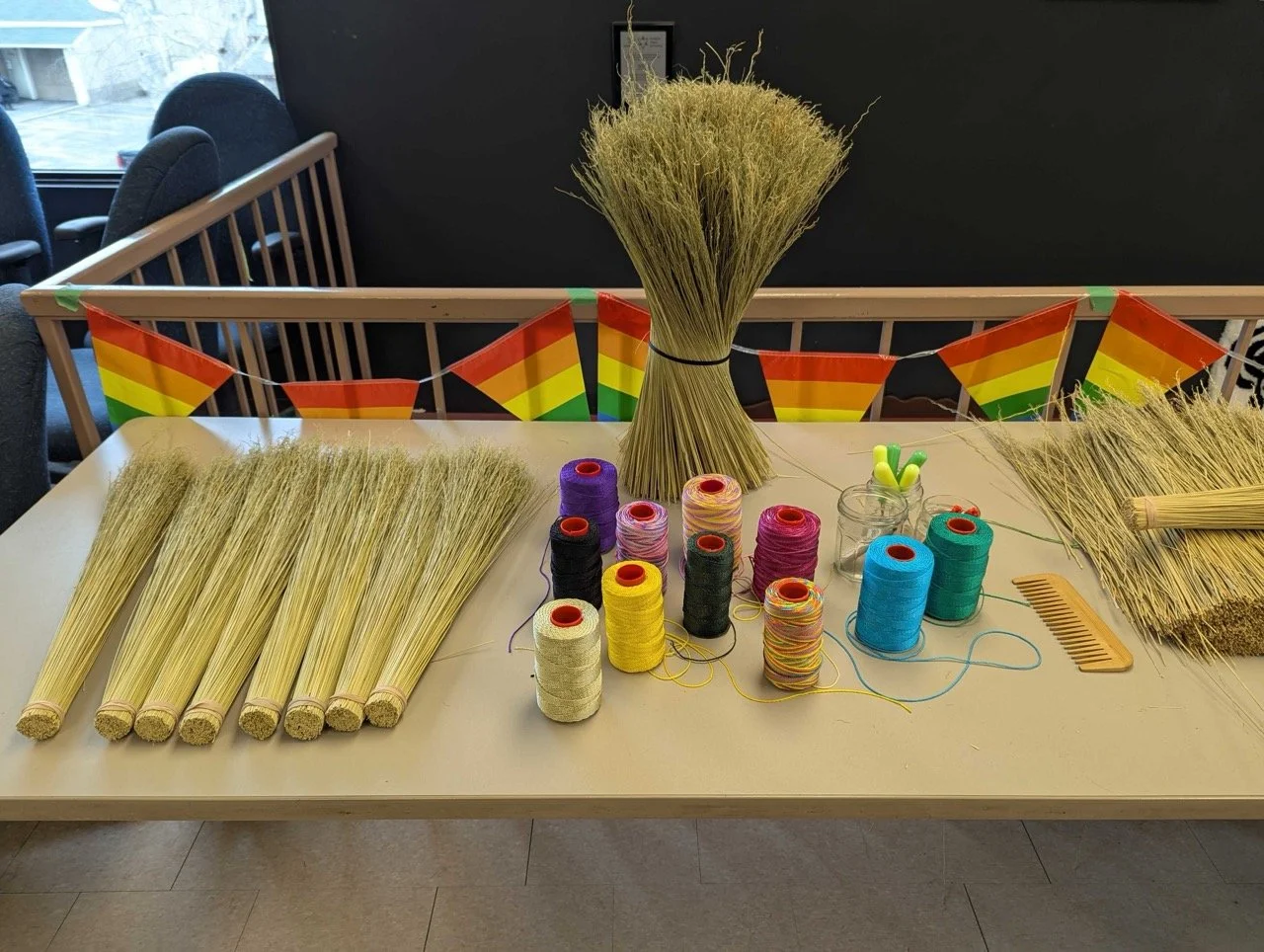 A table decorated with wheat and yarn, with small rainbow flags in the background.