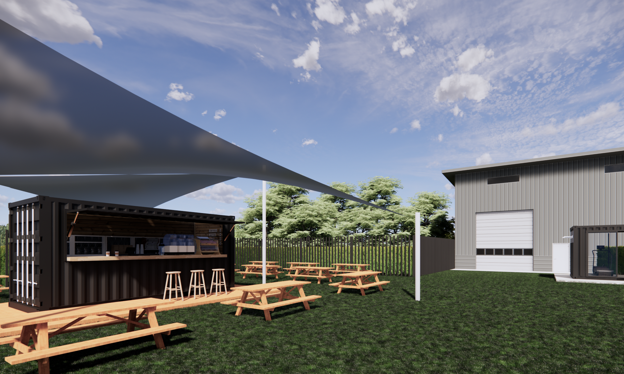 An outdoor seating area with picnic tables under a large shade sail, a small black food or drink stand, a metal building with a garage door, and a grassy yard with trees in the background under a partly cloudy sky.