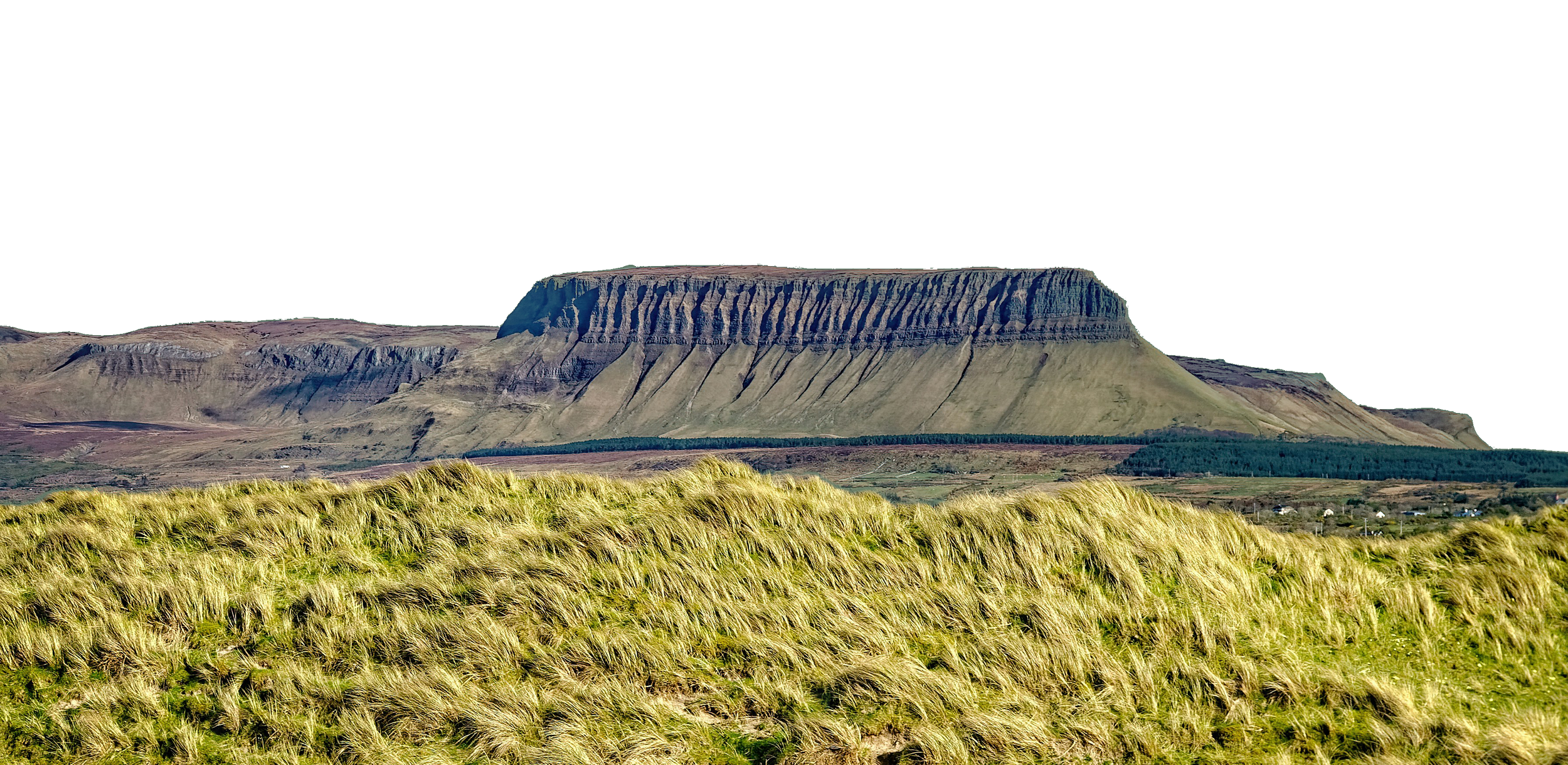A large plateau mountain with steep sides and a flat top, viewed from a grassy field in the foreground, under a black sky.