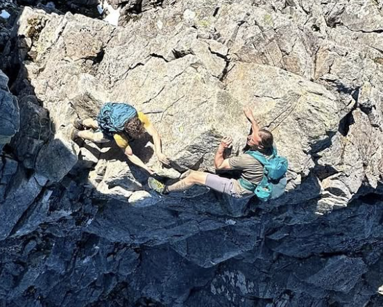 Two climbers on a rocky mountain face, one assisting the other during rock climbing
