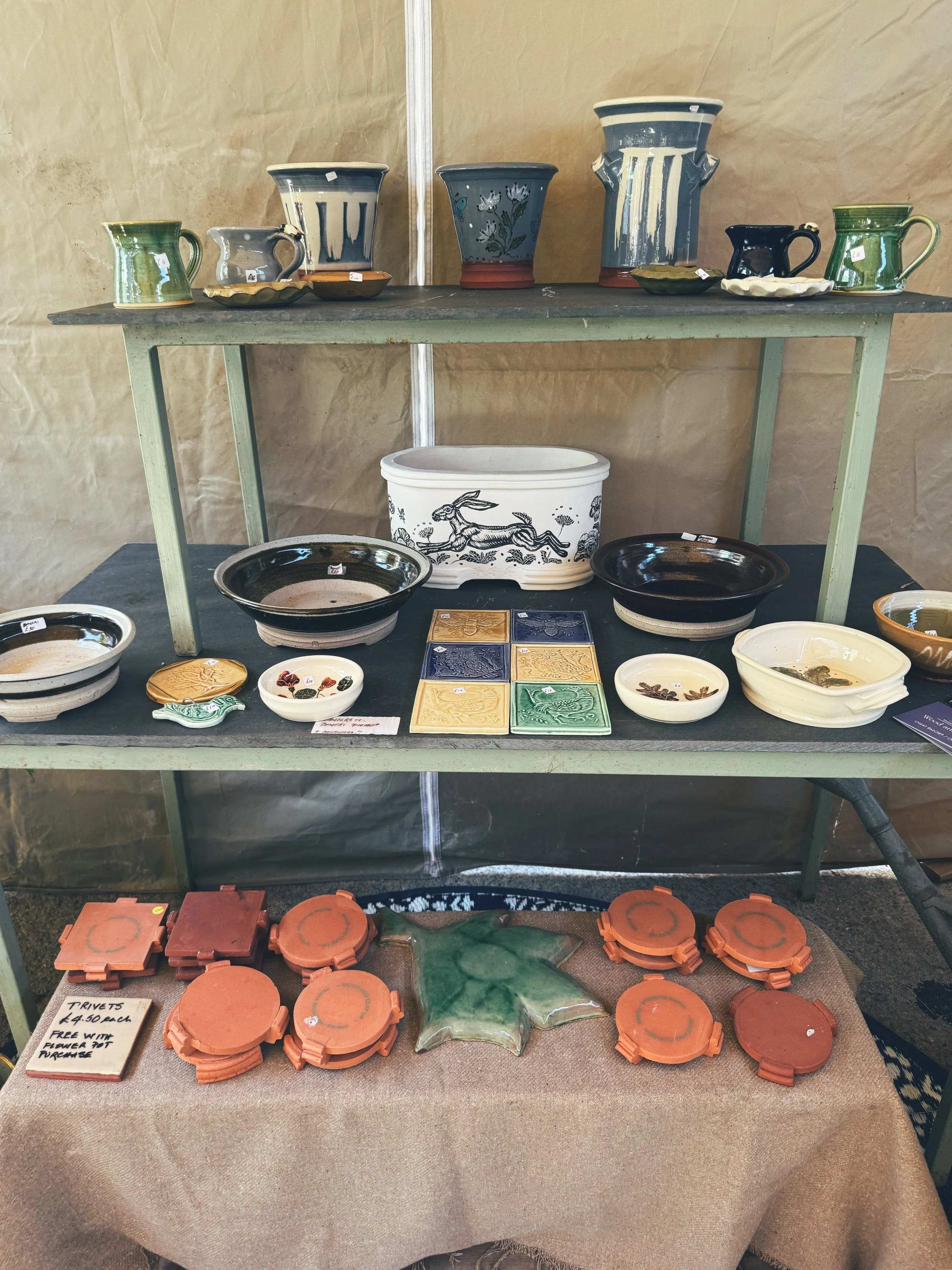 Display of ceramic pottery and kitchenware at a market stall, including bowls, mugs, tiles, and decorative items in various colors and designs.