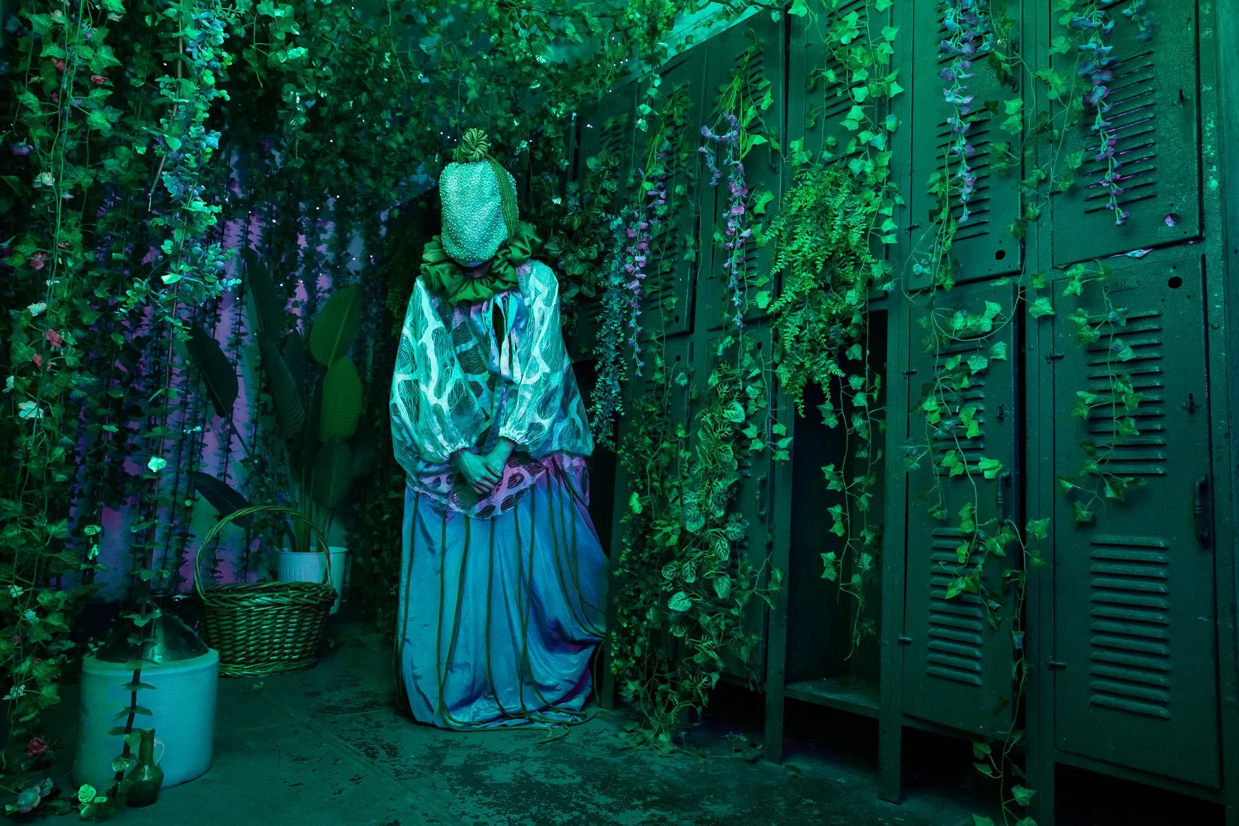Costumed BOTO performer standing among artificial vines and lockers in a Gymnopedie installation room.