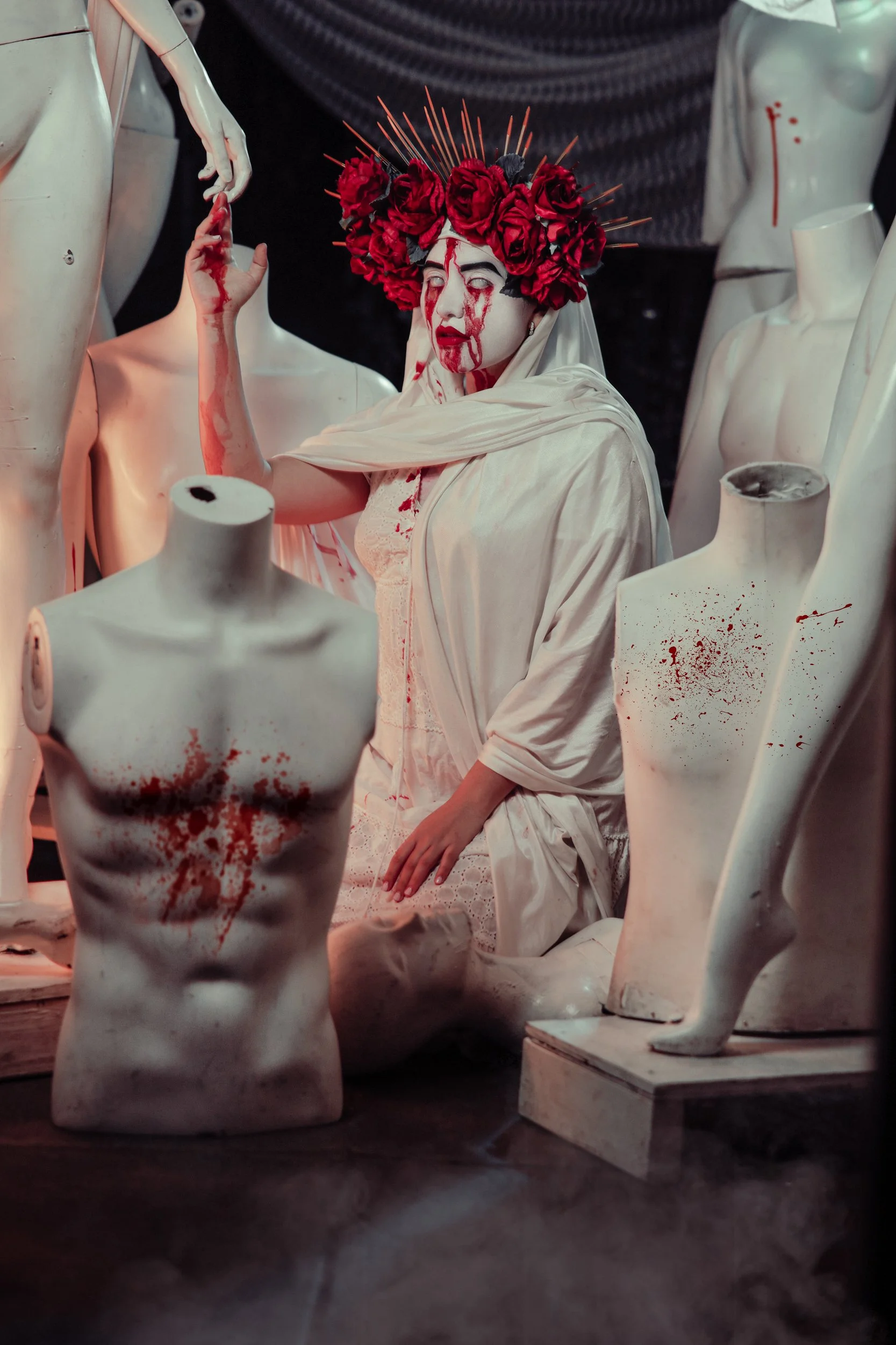 Macabre performer with bloody face and headpiece made of roses surrounded by mannequins at Gymnopedie