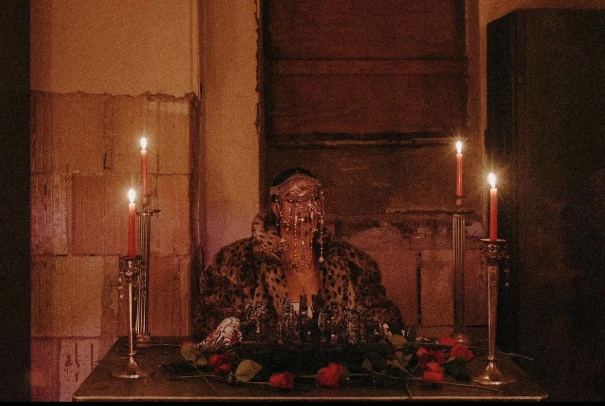Model wearing designer headpiece seated in a candlelit, distressed room inside Gymnopedie’s basement venue.