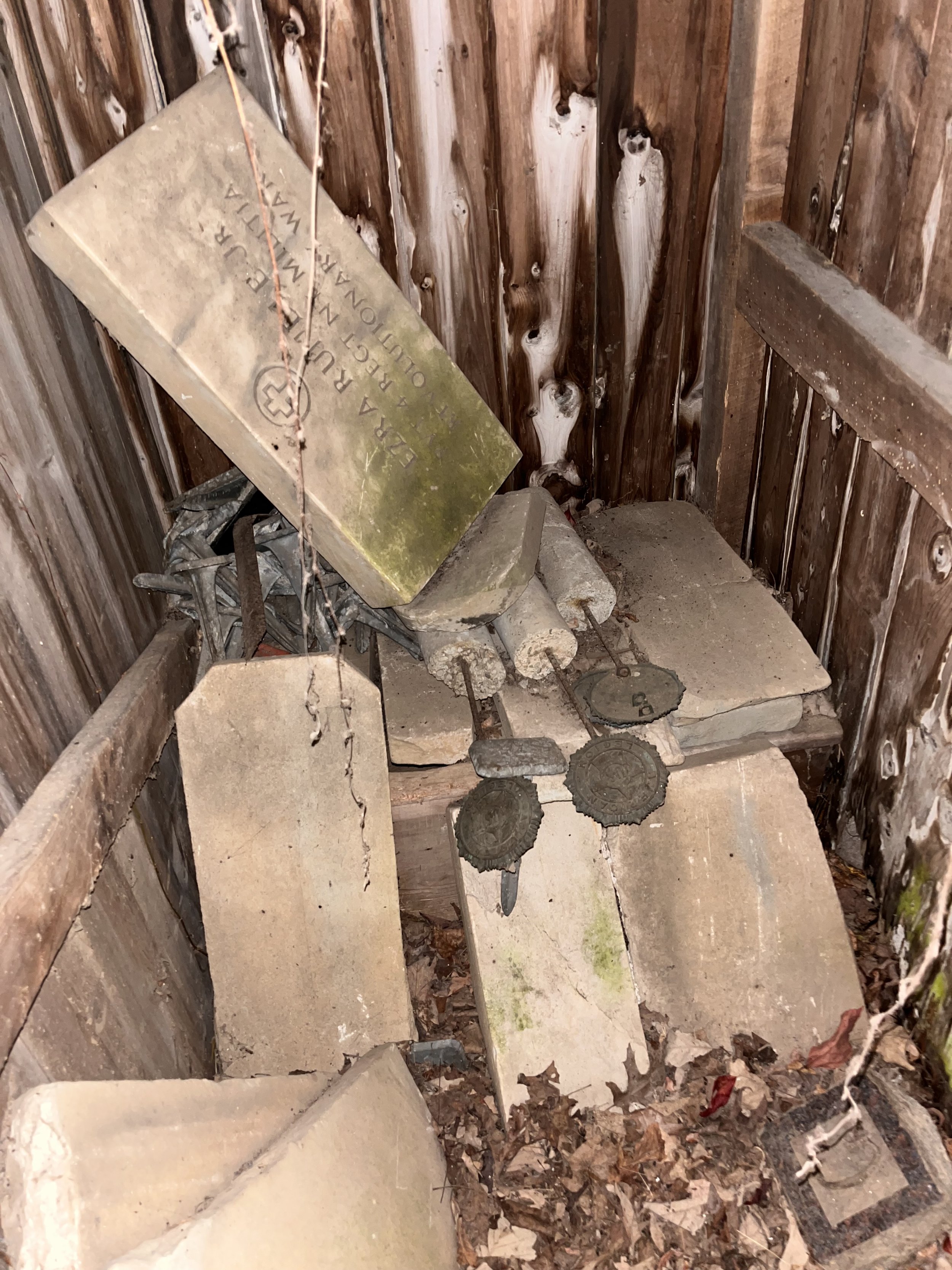 weathered cemetery markers and broken headstones stored carelessly in a shed