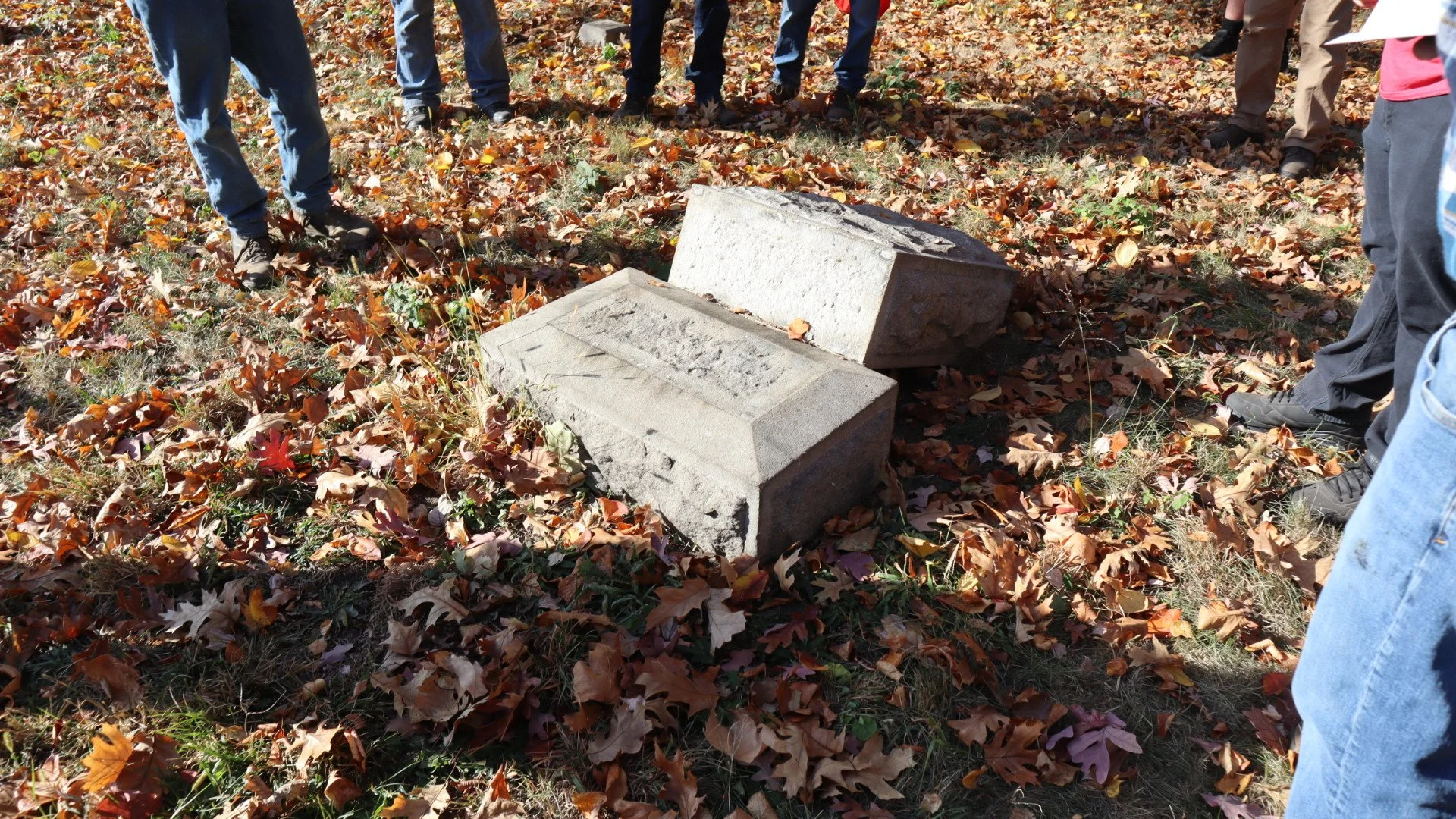 Broken concrete blocks in a park surrounded by fallen autumn leaves, with people standing around.