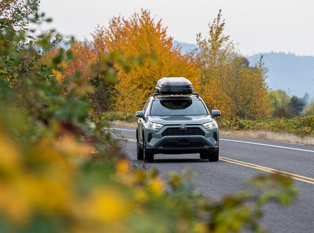 An SUV driving on a mountain road with a Yakima Skybox cargo box