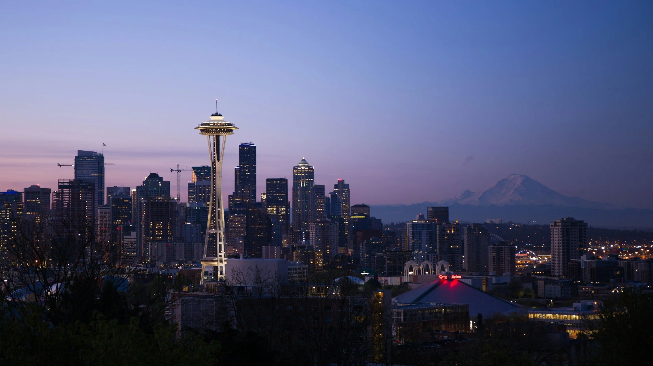 Seattle skyline at dusk with the Space Needle in the foreground and Mount Rainier in the background.