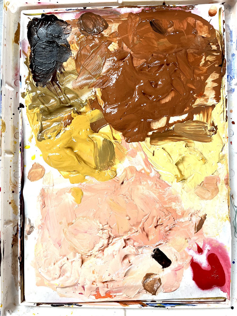 Mixed oil paint colors on a palette, including black, brown, yellow, pink, and red.