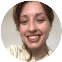 A young woman smiling with light-colored hair and wearing a light-colored shirt.