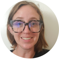 A woman with blonde hair, glasses, and a friendly smile taking a selfie indoors.