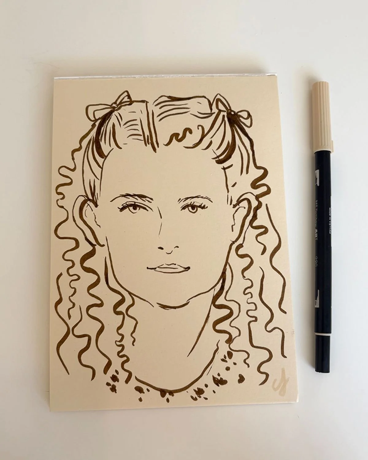 Line drawing of a woman with curly hair and bows, wearing a necklace, on an off-white paper next to a black marker.