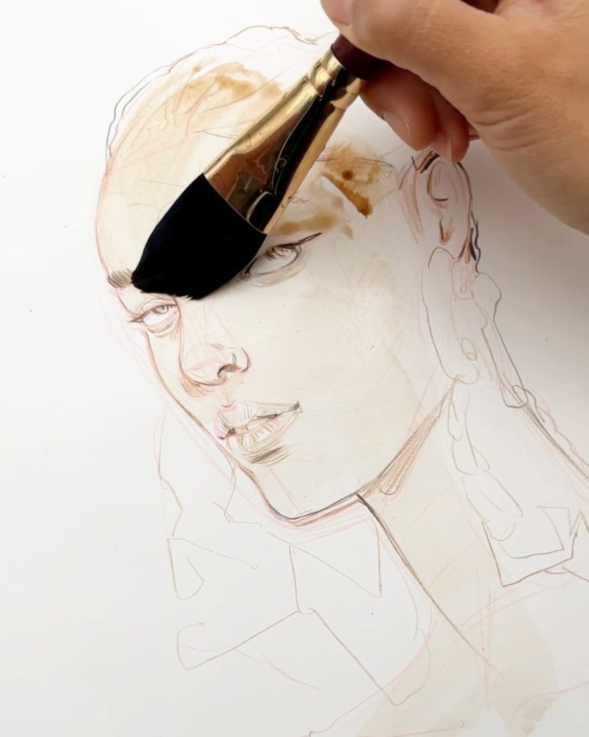A hand holding a paintbrush, working on a detailed sketch of a woman's face on paper.