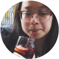 Person drinking a dark-colored beverage through a straw.