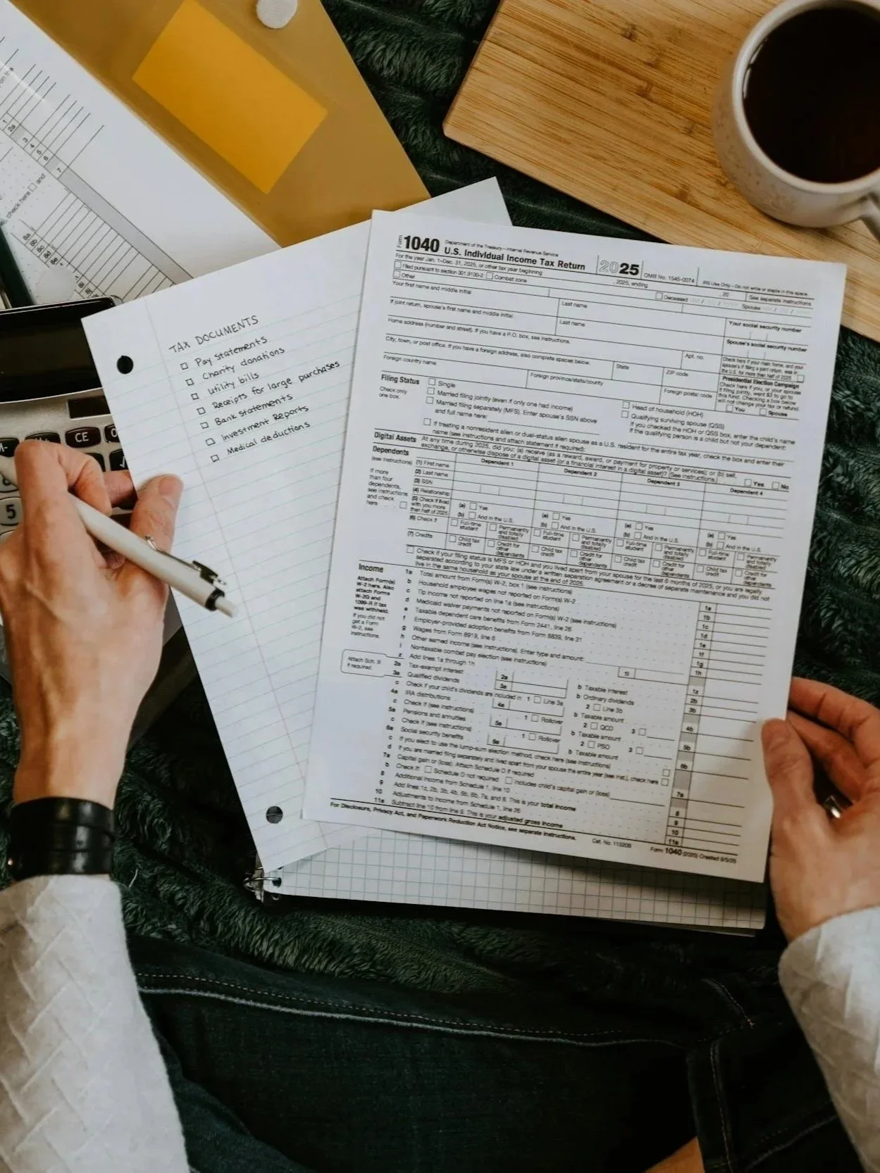 Bend, Oregon, Oregon, Pacific Northwest, Person filling out a tax form titled '1040 U.S. Individual Income Tax Return' surrounded by documents, a coffee mug, and a wooden board on a black textured surface.