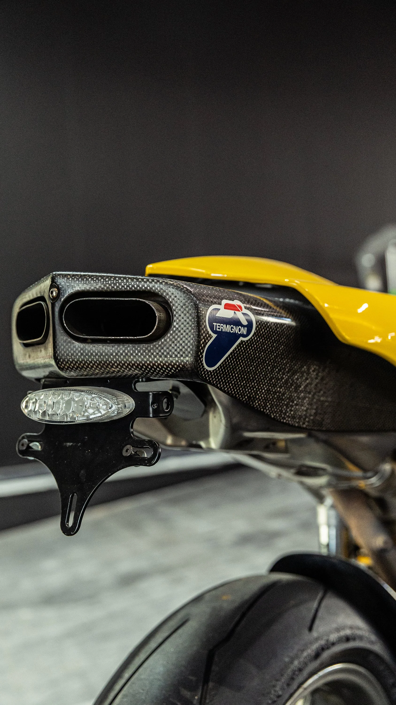 Particolare del posteriore di una motocicletta con tubo di scarico in fibra di carbonio e ruota.