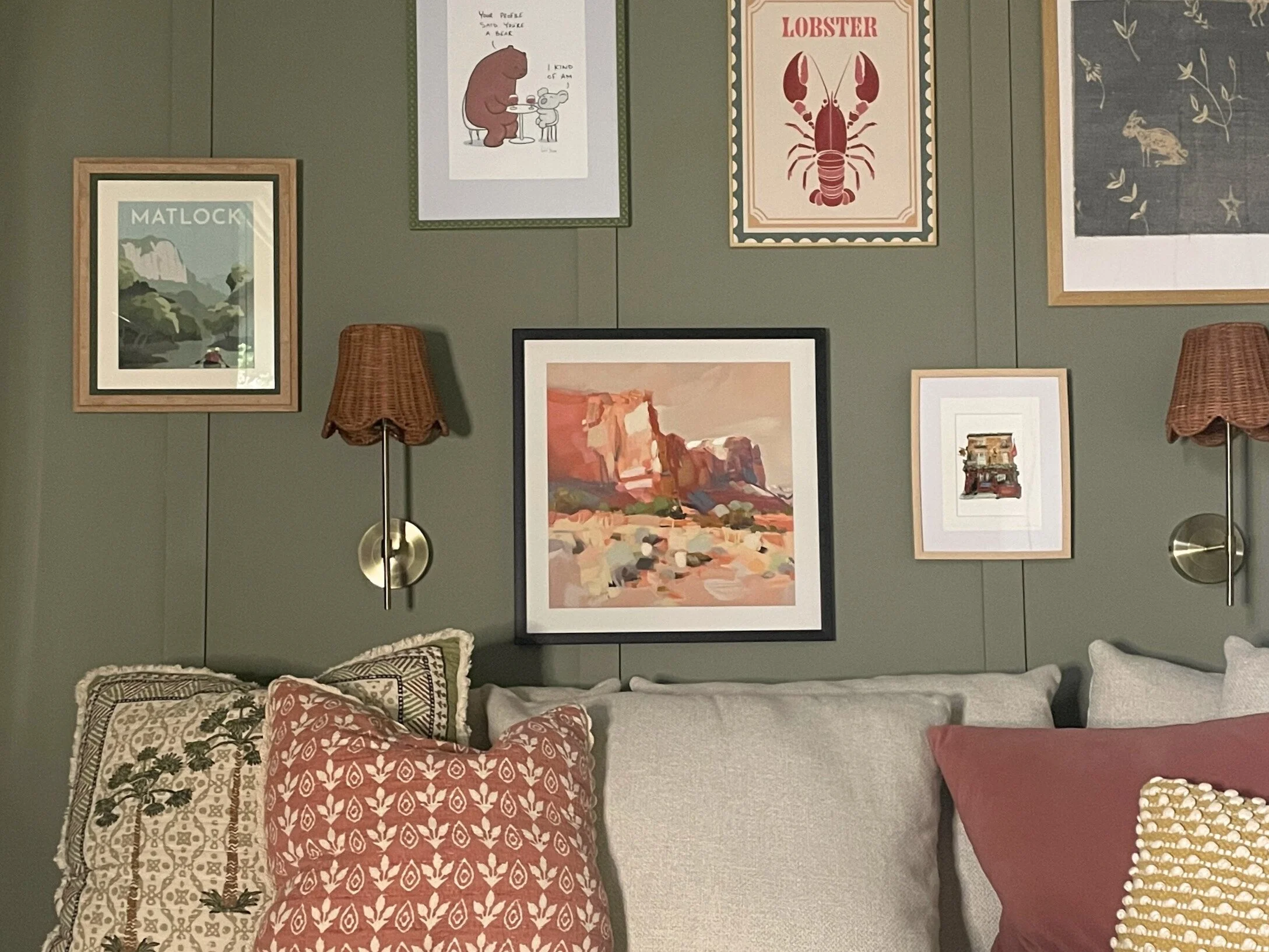 Sage green panelled sitting room with a framed gallery wall and terracotta cushions