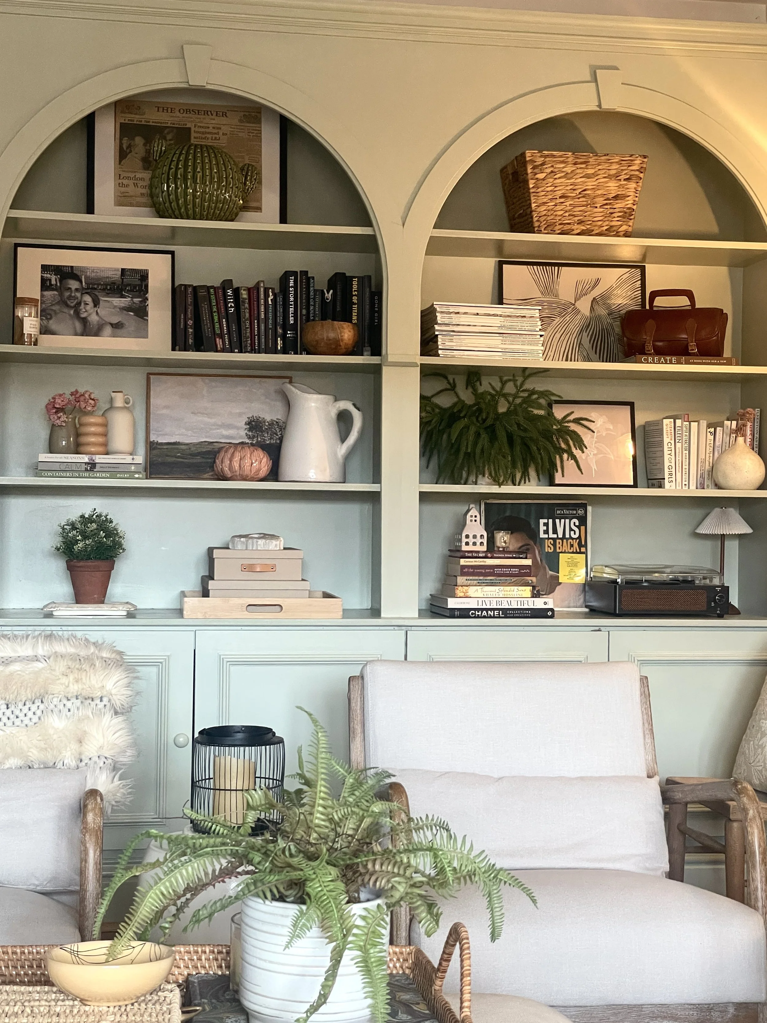 Arched built-in shelving in sage green, styled with books, baskets and plants
