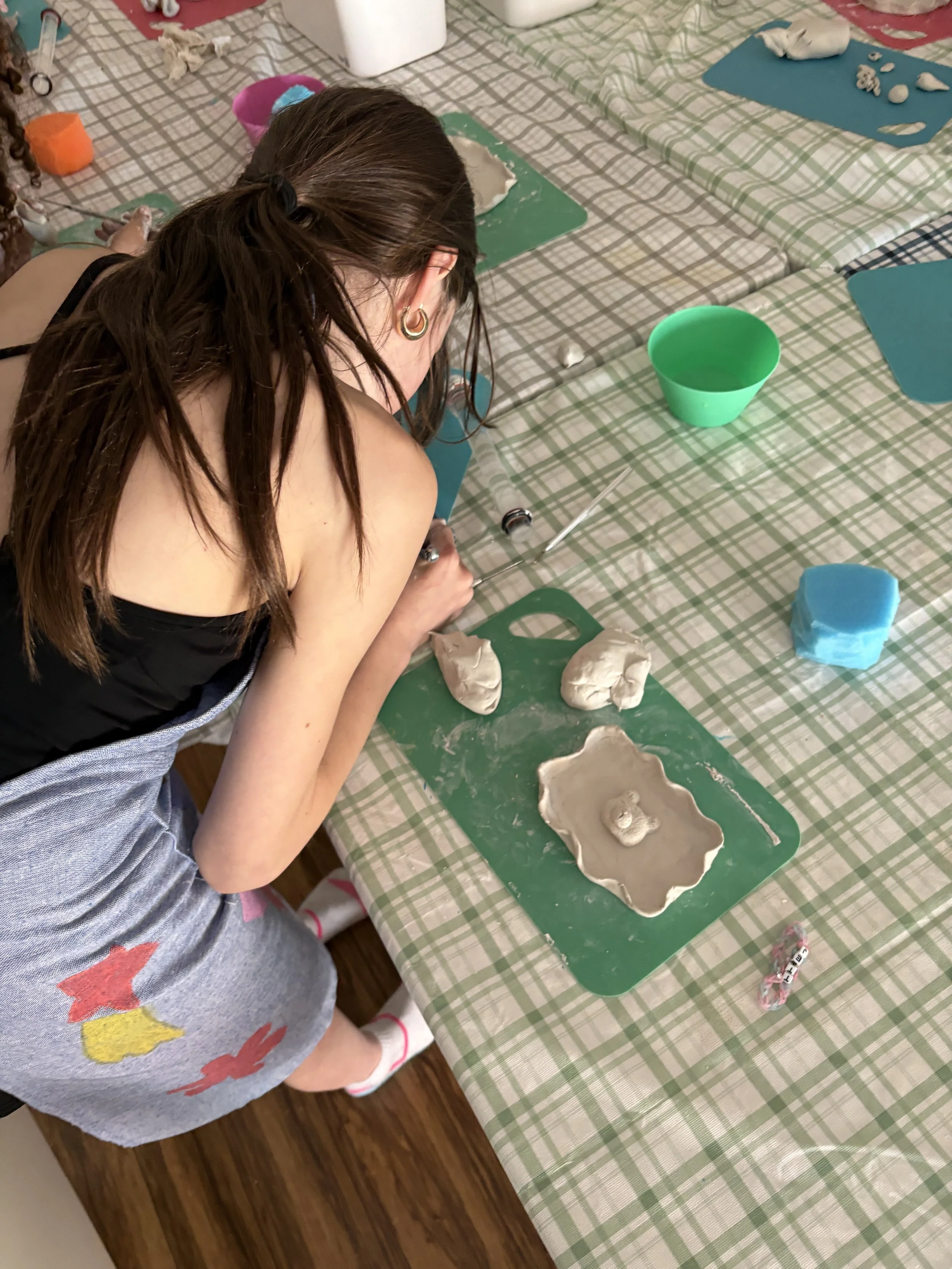 A long haired kid working with clay to make a trinket tray