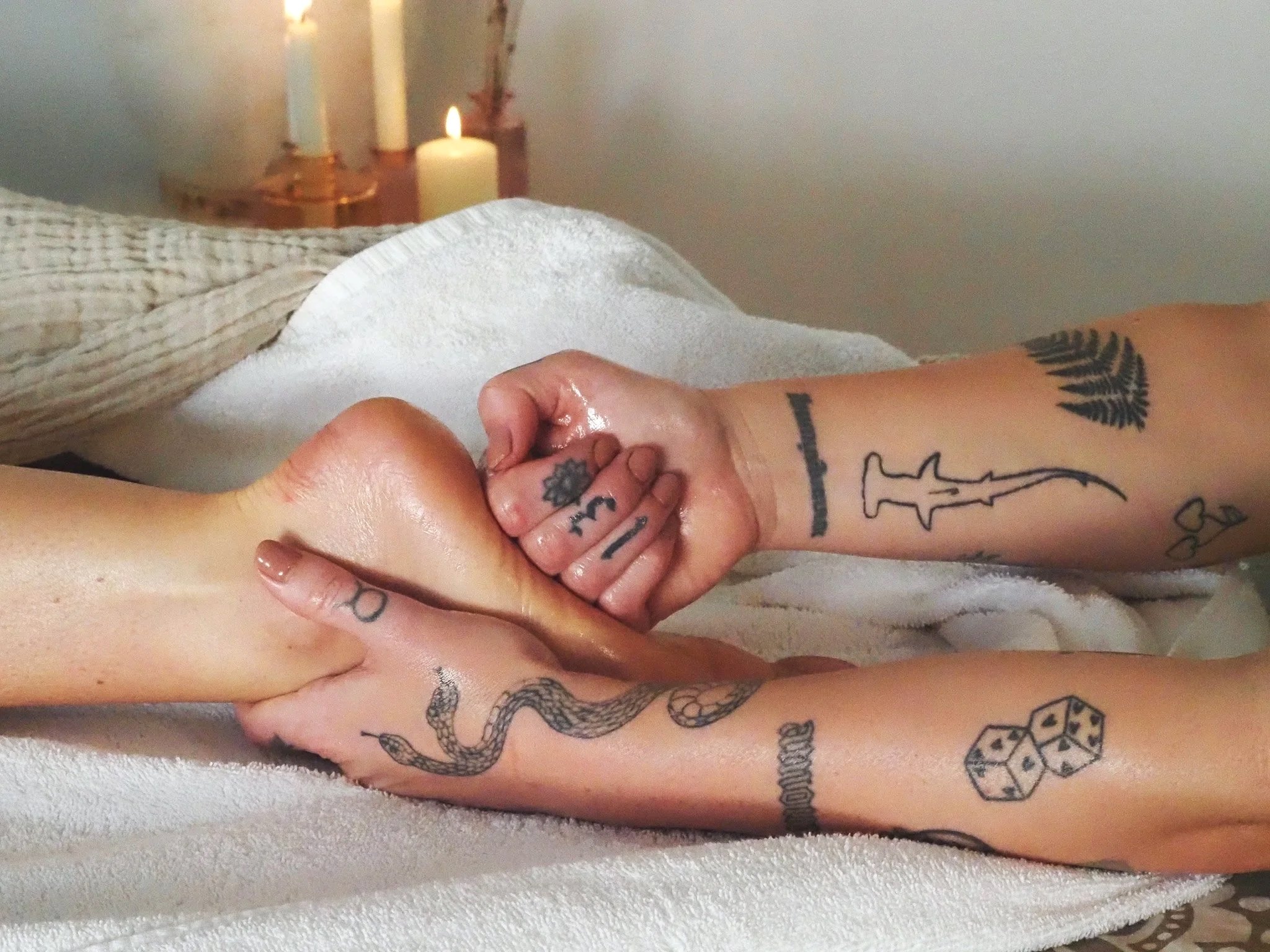Close-up of a person receiving a reflexology massage, with their foot resting on a white towel. In the background, there are lit candles placed on a surface.