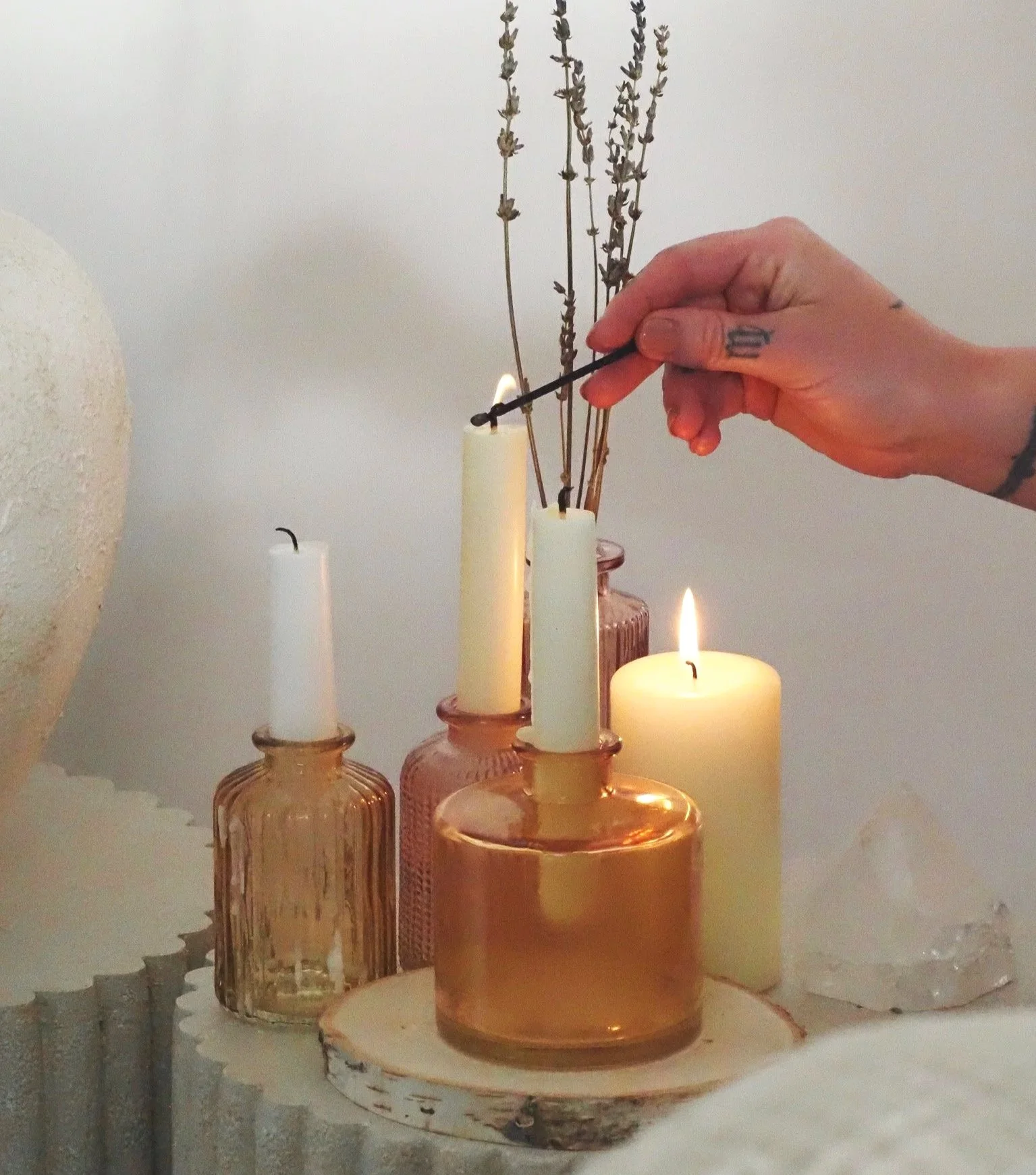 Person lighting a candle with a match in a room with several candles and dried lavender in the background.
