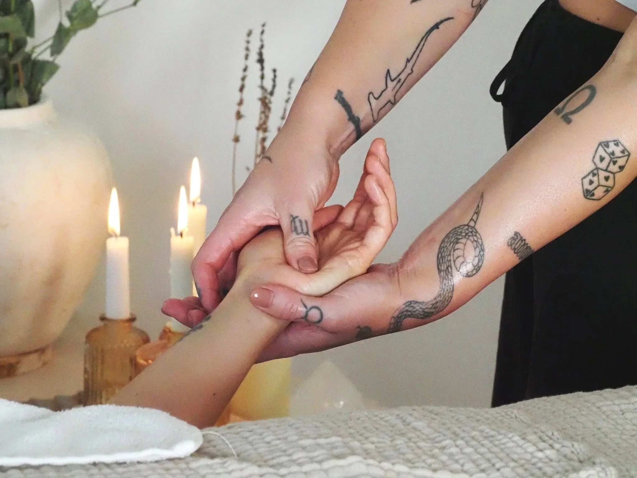 A person receiving a massage at a spa with lit candles and a large vase in the background.
