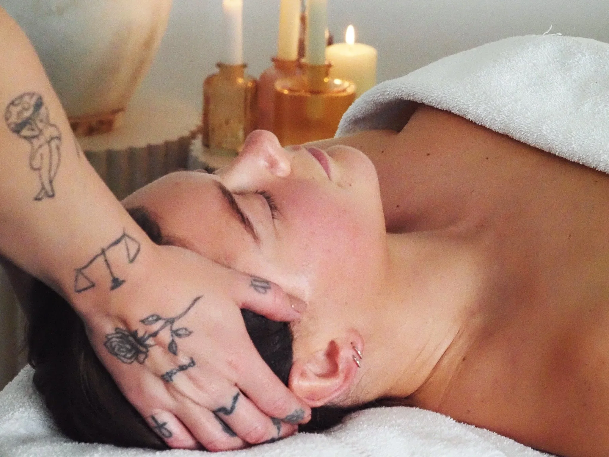 A woman receives a massage, lying down with her eyes closed, covered with a towel.