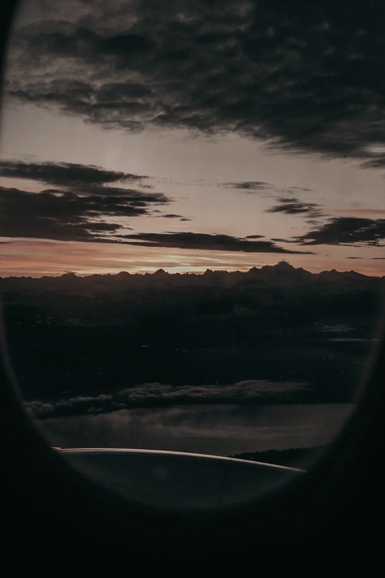 Sunset view with dark clouds over mountain silhouette, seen through airplane window