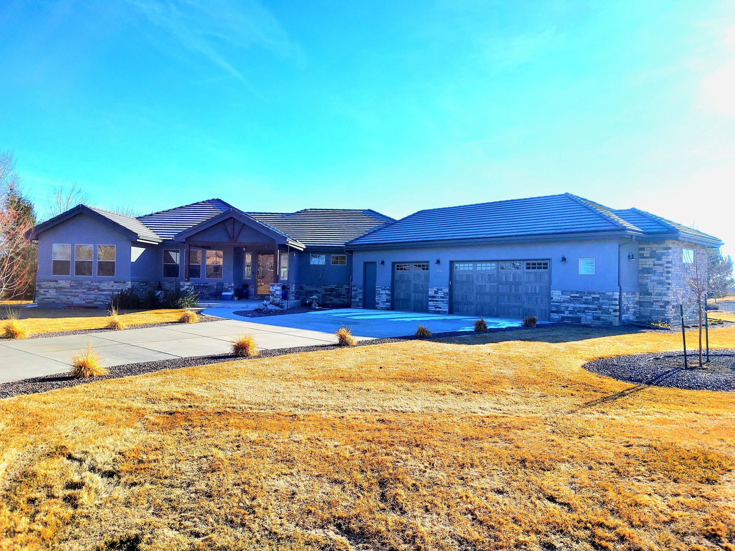 A modern house with a stone and stucco exterior, large windows, three-car garage, and a landscaped front yard under a clear blue sky.