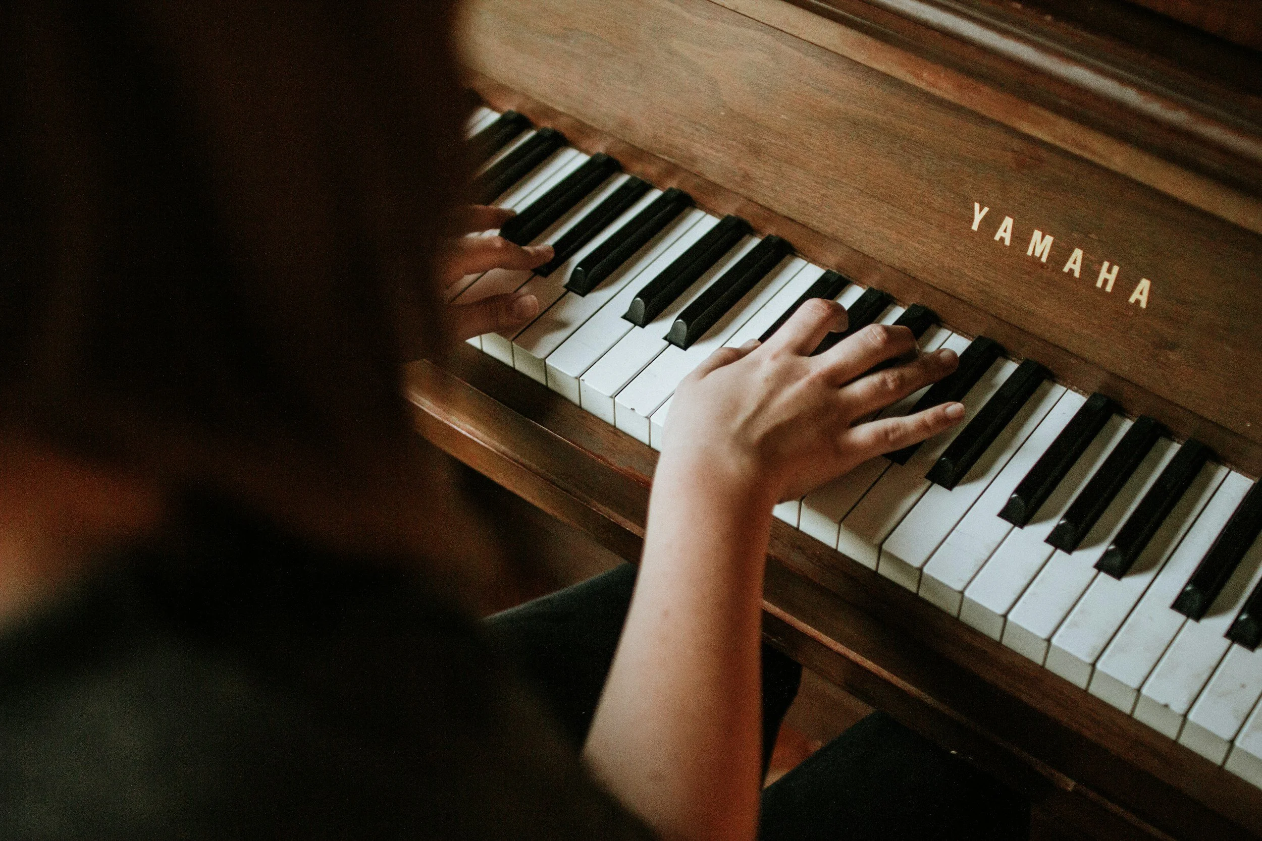 Child playing a Yamaha upright piano, focusing on hands pressing the keys.